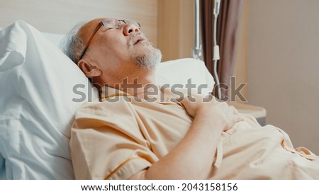 Sad senior Asia man having having heart attack lying on hospital bed and press emergency button. Sick aged guy lying hospitalized in a medical clinic. Health insurance or hospitality concept. Royalty-Free Stock Photo #2043158156