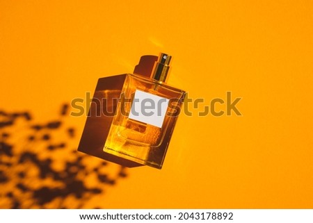 Transparent bottle of perfume on an orange background. Fragrance presentation with daylight. Trending concept in natural materials with plant shadow. Women's and men's essence. Royalty-Free Stock Photo #2043178892