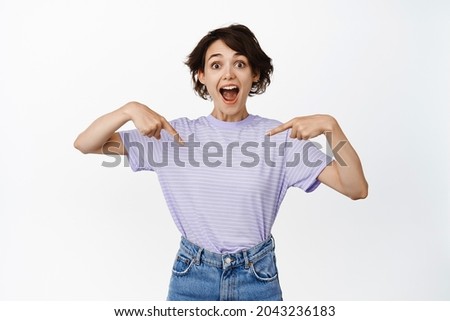 Portrait of impressed and excited young woman showing info on empty space, pointing fingers at your logo, banner or sale promotion, standing over white background