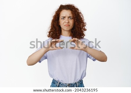 Frustrated curly woman frowning, grimacing upset, showing credit discount card, standing in summer t-shirt over white background