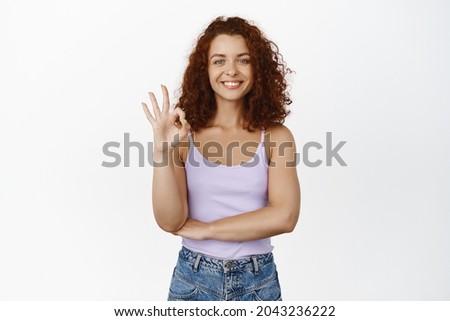 Okay, very good. Smiling redhead girl showing OK sign in approval, pleased, praise you, recommending smth, make compliment, white background