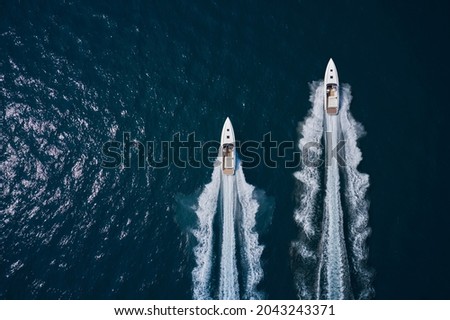 Speed boats movement on the water. Speed boats on dark blue water aerial view. Two speed boats moving fast on dark blue water.. Large white boat driving on dark water. Royalty-Free Stock Photo #2043243371