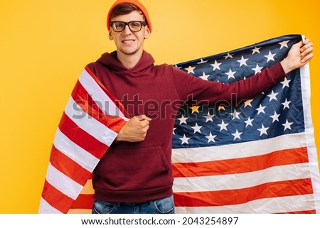 handsome guy with an orange hat on his head with glasses and a red witer, holding moisture in his hands, 4th of july america day