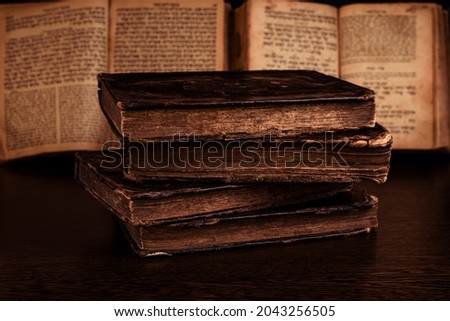 Stack of old worn shabby jewish books in leather binding and open blurred Torah in the background in the dark. Closeup. Selective focus Royalty-Free Stock Photo #2043256505