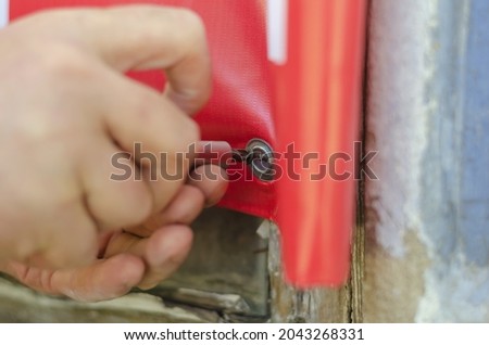 An adult man attaches an advertising banner to the facade of an old building. A hand screws down a red advertising sign. Informational large-format products. Selling real estate. Selective focus.
