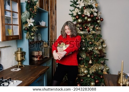 Young smiling woman in a sweater, winter holidays in decorated home interior with Christmas tree.