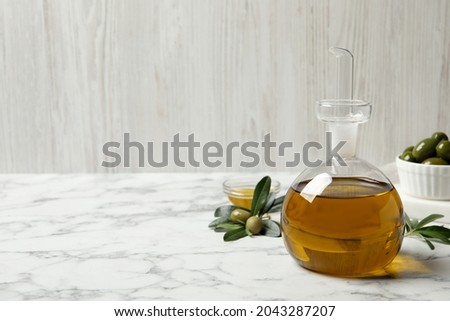 Glass jug of oil, ripe olives and green leaves on white marble table. Space for text