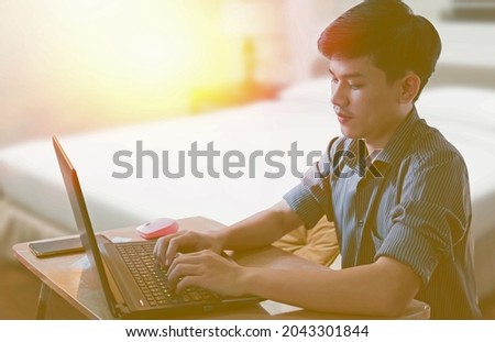 A young man wearing a black striped shirt sits at work, using a notebook to communicate.