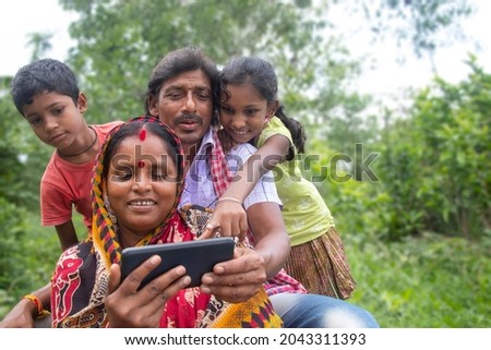 Indian Rural Parents and their two children watching movie in agricultural field Royalty-Free Stock Photo #2043311393