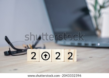 Wooden blocks with the inscription 2022 with an up arrow placed on office desk. Blurry office desk background. Business and economy growth and development in the year of 2022 concept. 