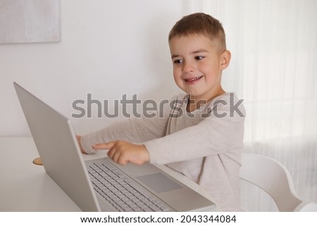 Happy little boy playing game on laptop at home. Portrait of a child at home watching cartoon on the computer. Modern kid and education technology.