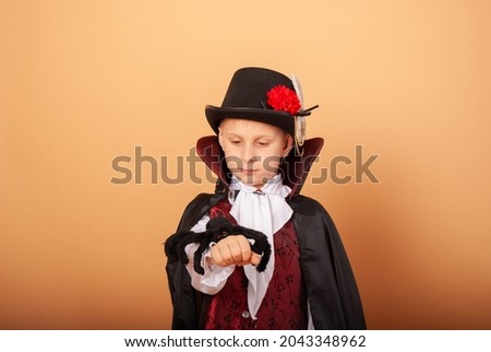 American-looking boy with a spider in his hands dressed as Count Dracula vampire