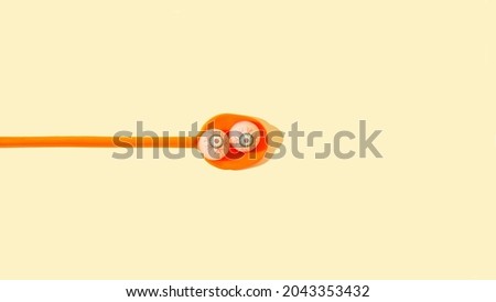 An orange spoon with two scary eye balls on pastel yellow background. Minimal Halloween spooky meal concept. Halloween banner with copy space.