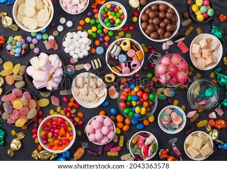 Pink lollipop candies in jar with various milk chocolate and jelly gums candies on black with liquorice allsorts and strawberry bonbons and large variety of sweets and candies. Royalty-Free Stock Photo #2043363578