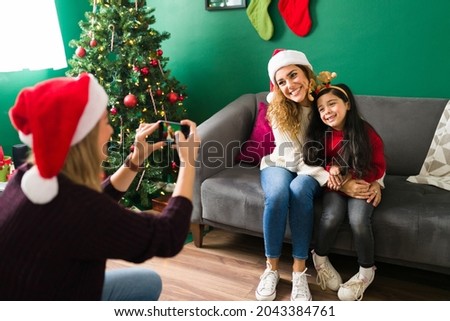 Happy woman taking a picture with a smartphone to her caucasian wife and daughter during Christmas eve 