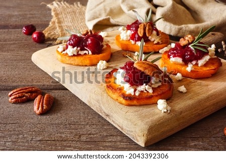Fall sweet potato crostini appetizers with cheese, cranberries and pecans on a wooden platter. Table scene with a rustic wood background. Royalty-Free Stock Photo #2043392306