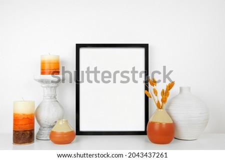 Mock up black frame with autumn home decor on a white shelf. Fall concept. Portrait frame against a white wall.