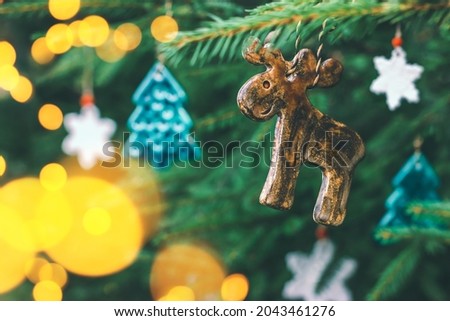 Unusual ceramic toys in the shape of an elk, a Christmas tree and snowflakes hang on a spruce branch. Decorations for the new year, festive mood