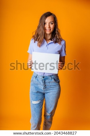 a young beautiful blonde in a blue T-shirt and jeans holds a white sheet of paper in her hands. copy space.