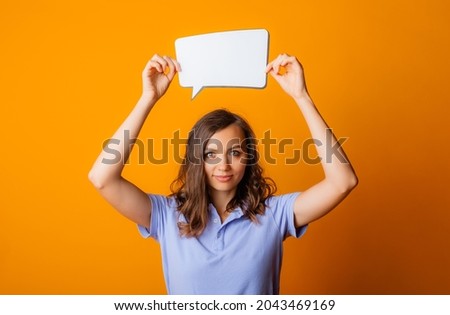 Happy young woman holding empty speech bubble on yellow background.