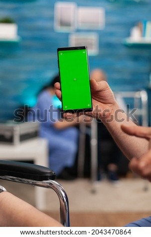 Close-up of man social worker looking at mock up green screen chroma key with isolated display while nursing disabled senior woman at home. Social services nursing elderly retired female. Support