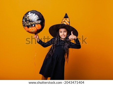 A cheerful girl in a witch costume is holding a balloon with the inscription Halloween. halloween concept.