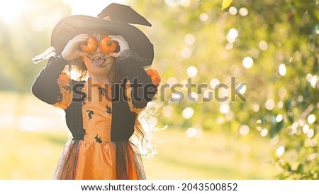 Little witch girl indulges and has fun with two little pumpkins on Halloween.