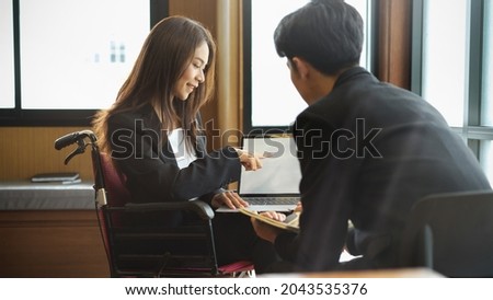 Attractive asian businesswoman in wheelchair working with colleagues in office, discussing project on laptop computer. laptop blank screen mockup