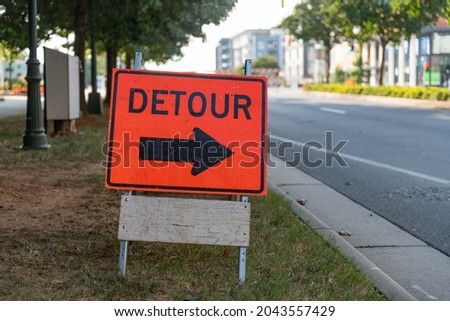 Orange and black detour sign with bold arrow on a city street