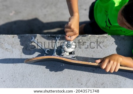Top view of a concentrated child repairing his skateboard before using it inside the skateboard park on a sunny day. High quality photo