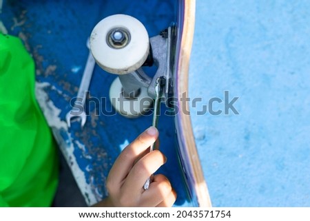 Close up of a child repairing the wheel of his skateboard after using it in the skateboarders' park. High quality photo