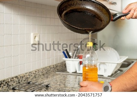 Man placing recycled edible oil from a frying pan into a plastic bottle in his home kitchen. Recycle at home concept. High quality photo Royalty-Free Stock Photo #2043571757