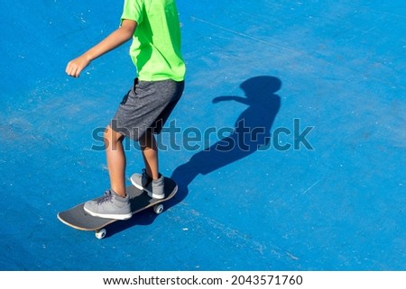 Child on skateboard on the blue background of a skateboarders' park on a sunny day where the full shadow is reflected on the ground. High quality photo