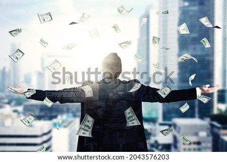 Double exposure of male manager outstretched his arms while standing under falling dollar money with modern city background