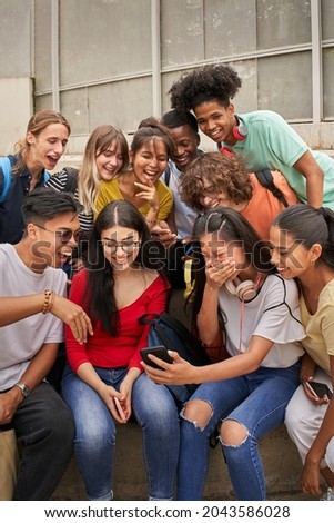 Vertical photo of a multi-ethnic group of students using cell phone and laughing. Teenagers using a smart phone, surfing the web. Having fun together. Royalty-Free Stock Photo #2043586028