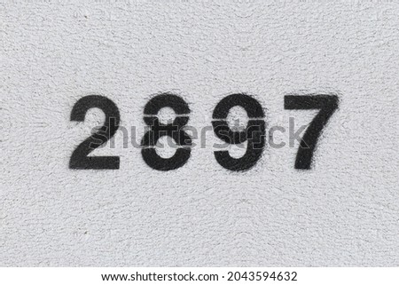 Black Number 2897 on the white wall. Spray paint. Number two thousand eight hundred and ninety seven.