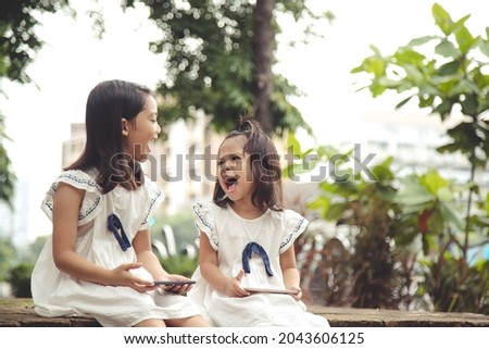 Concept kids and gadgets. Two little girls siblings sisters look at the phone and smile. They hold a smartphone watch videos, learn, play games, speak online. Internet for children. Parental control