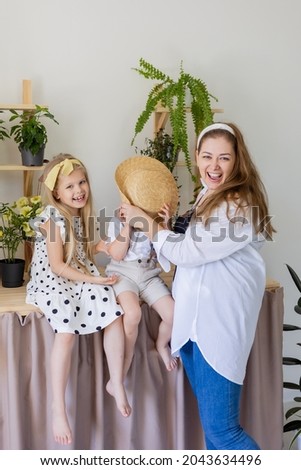 a young mother with her son and daughter laughs, hugs and plays indoors with home flowers. a girl and a boy are sitting. Concept of a happy, fun family. Lifestyle, space for text. High quality photo