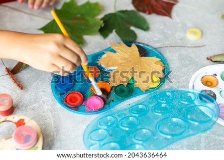 Child painting autumn leaves at home