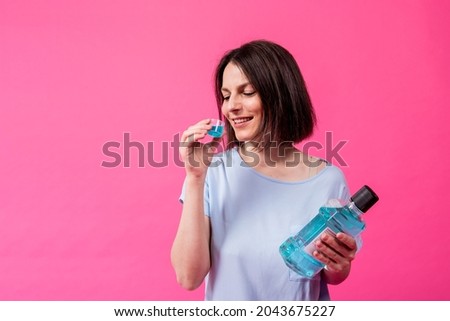 Beautiful girl uses mouthwash on the pink background Royalty-Free Stock Photo #2043675227