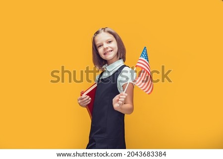 Cute smiling caucasian schoolgirl holding american flag and book on yellow studio background. Flag USA 