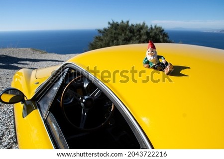 porcelain gnome lying on the hood of a yellow car with the sea in the background