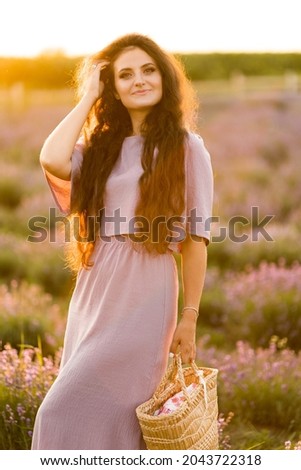 Portrait of stylish gorgeous female walking at the field, posing, looking at the camera. Brunette woman with picnic basket spending weekends outdoors, beautiful nature concept