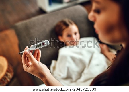 The child has a high fever. Mom looks at the thermometer, measures her daughter's temperature. Royalty-Free Stock Photo #2043725303