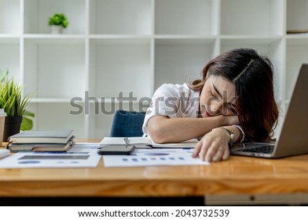 Asian woman napping at her desk, Businesswoman snoozing at her desk after working for a long time causing fatigue and sleepiness, she is resting. Hard work concept. Royalty-Free Stock Photo #2043732539