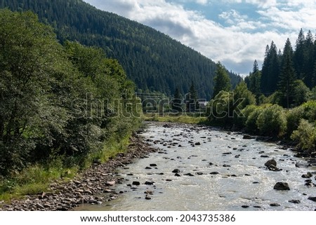 Beautiful landscape of lake with many stones, green and big trees and mountains on a hot sunny day in summer