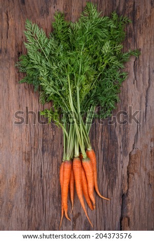 Bunch of fresh carrots with green leaves over wooden background 