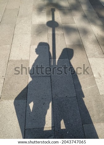 shadows of a boy and a girl leaning against a park lamp