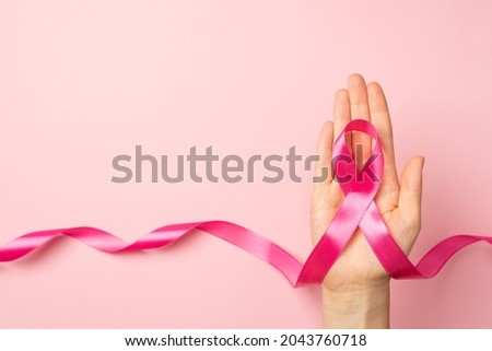 First person top view photo of female hand holding pink ribbon in palm symbol of breast cancer awareness on isolated pastel pink background with copyspace Royalty-Free Stock Photo #2043760718