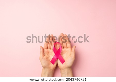 First person top view photo of girl's hands holding pink ribbon in palms symbol of breast cancer awareness on isolated pastel pink background with blank space